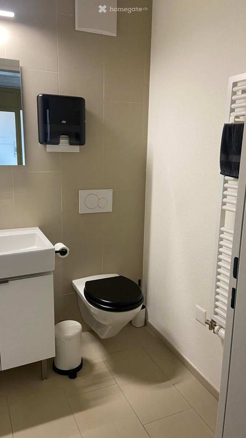 Modern bathroom with beige tiles, white sink, black toilet seat, radiator, and towel.