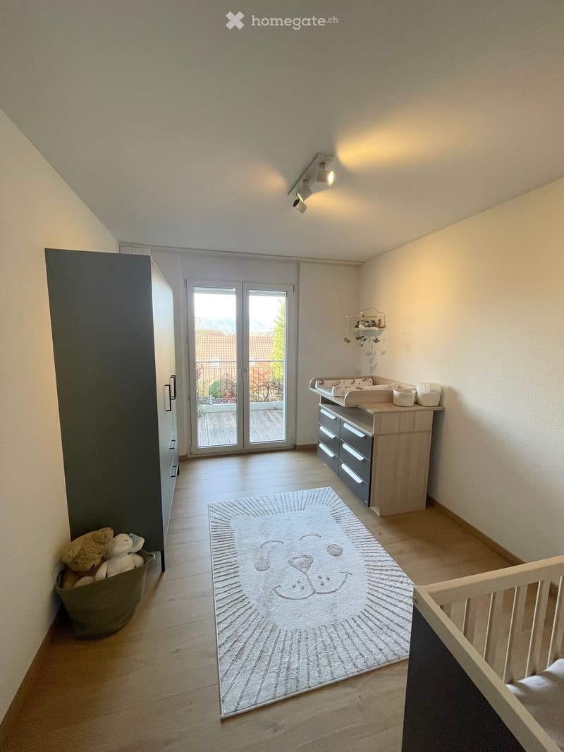 nursery with wooden floor, cabinet, baby bed, rug, sliding glass door, balcony