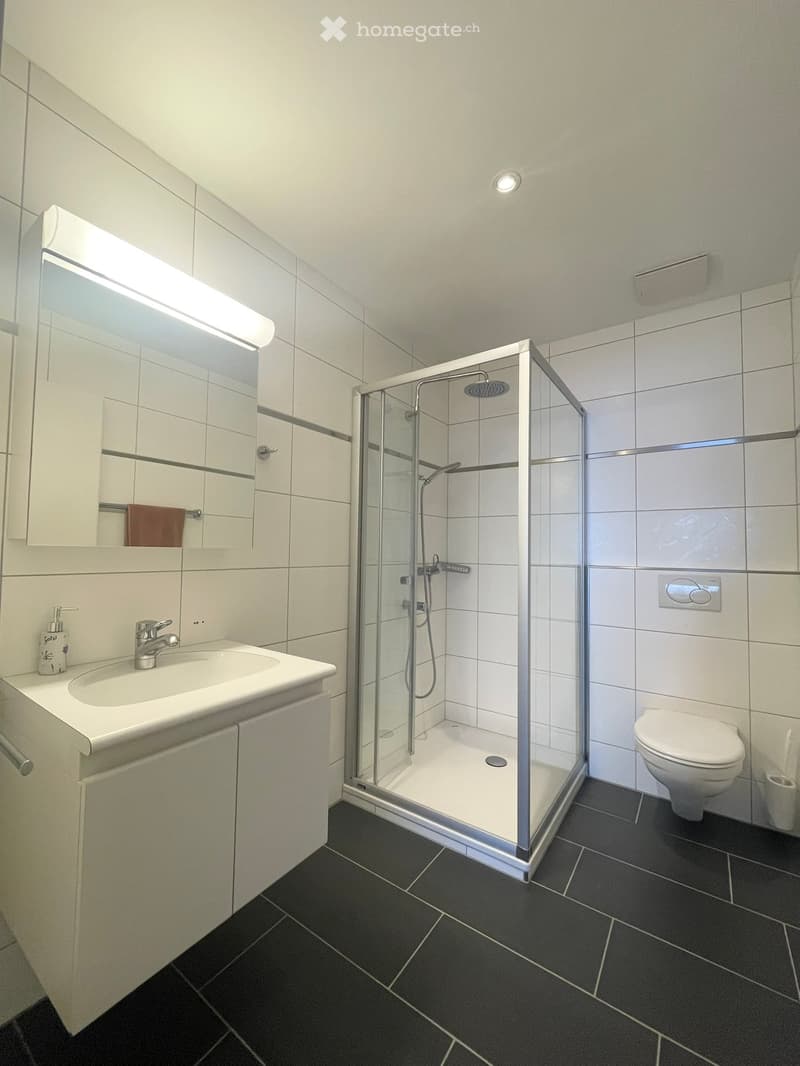 modern bathroom with white tiles, a glass shower, sink, and toilet