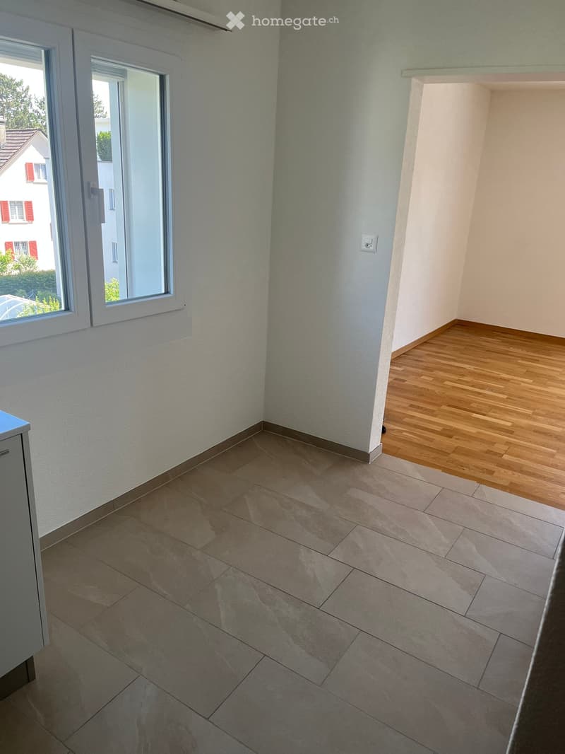 Empty room with light-colored walls, wooden flooring, and large windows offering a view of the outside. The space is clean and unfurnished.