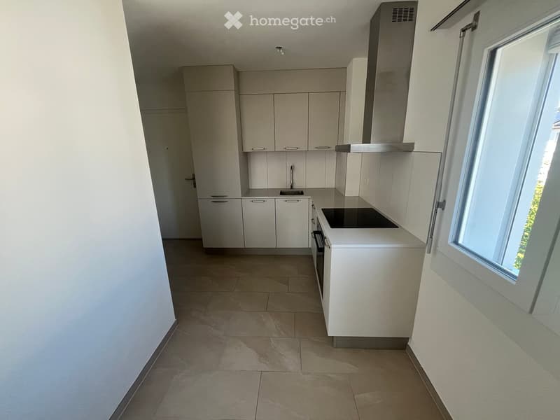 Modern, unfurnished kitchen with light-colored cabinets, a sink, a stove, and an oven. The space is clean and bright with tiled flooring and large windows allowing natural light.