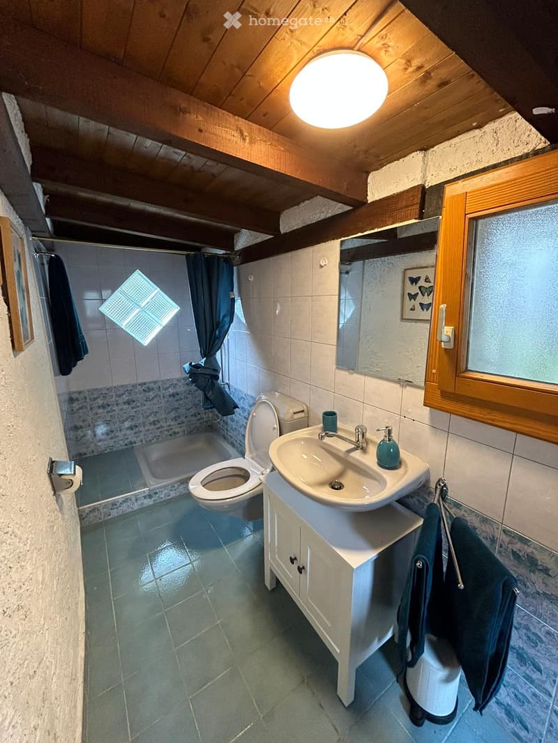 Cozy bathroom with a wooden ceiling, tiled walls, a sink with a cabinet, a toilet, a shower area with a curtain, and a framed picture on the wall.