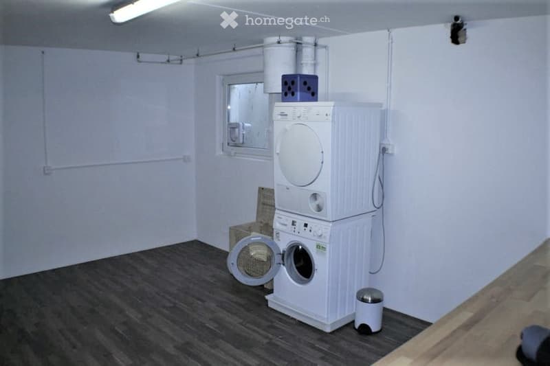 Bathroom with a private washing machine and dryer unit, a small trash bin, and a window with a mirror.