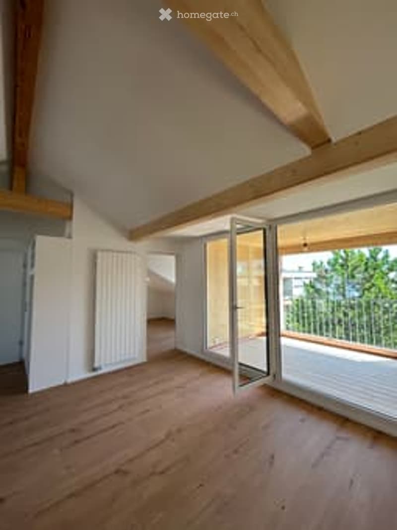 Bright, unfurnished room with wooden flooring, exposed wooden beams, large windows, and a balcony access door.