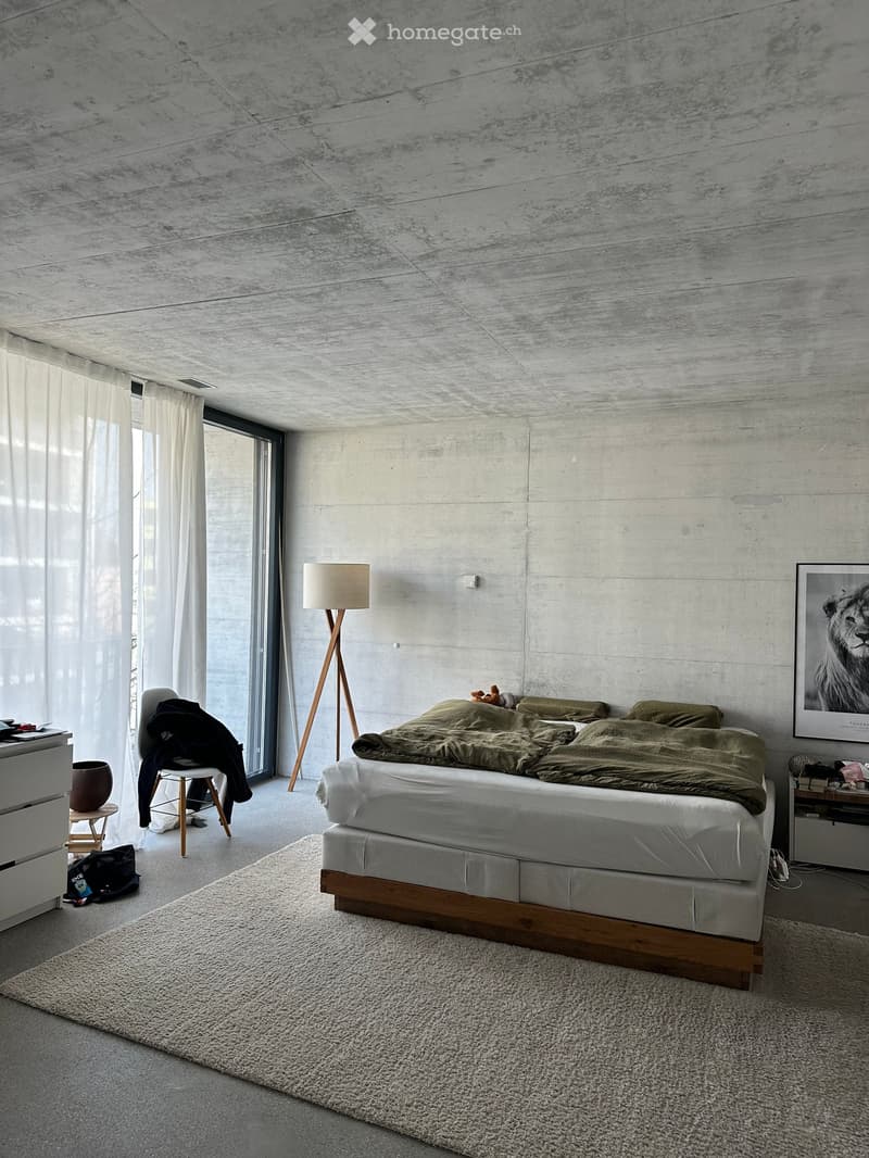 Modern bedroom with a large bed, green bedding, a floor lamp, a nightstand, a chair, and a picture frame on the wall.