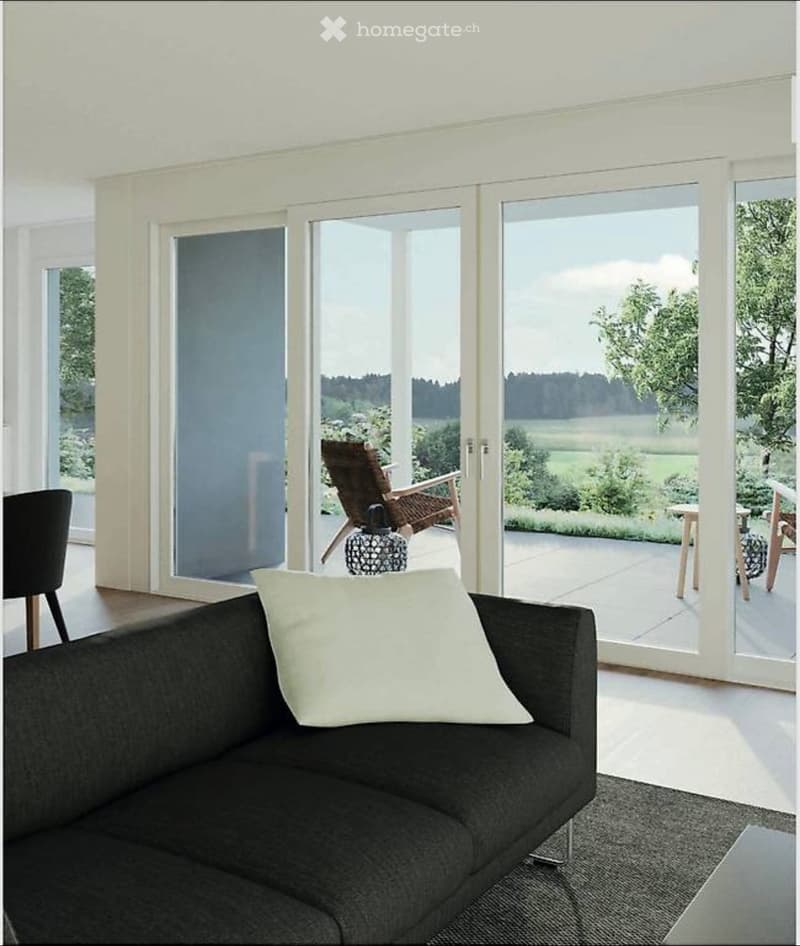 Modern living room with large sliding glass doors leading to a patio, featuring a dark grey sofa, a wooden chair, a small table, and a decorative plant.
