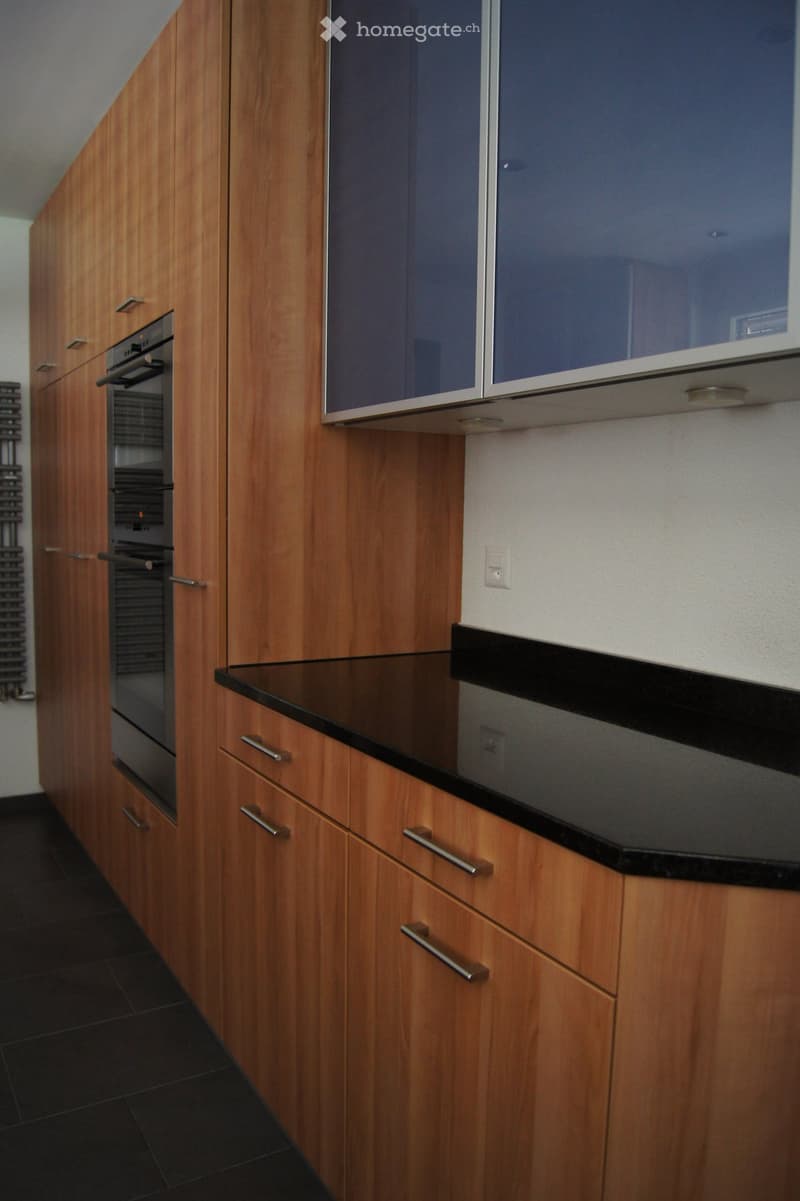 Modern kitchen with wooden cabinets, black countertop, and built-in oven. Features sleek design with metallic handles and a clean, contemporary look.