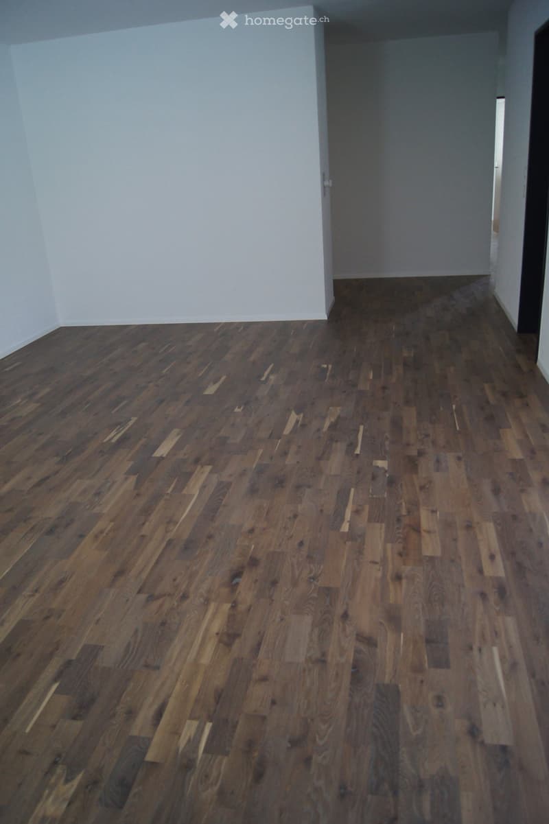 Empty room with wooden flooring and white walls, featuring a doorway leading to another space.