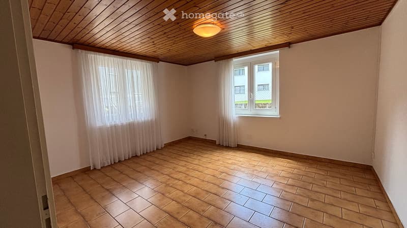 Empty room with tiled floor, wooden ceiling, and white curtains on windows. No furniture or equipment present.