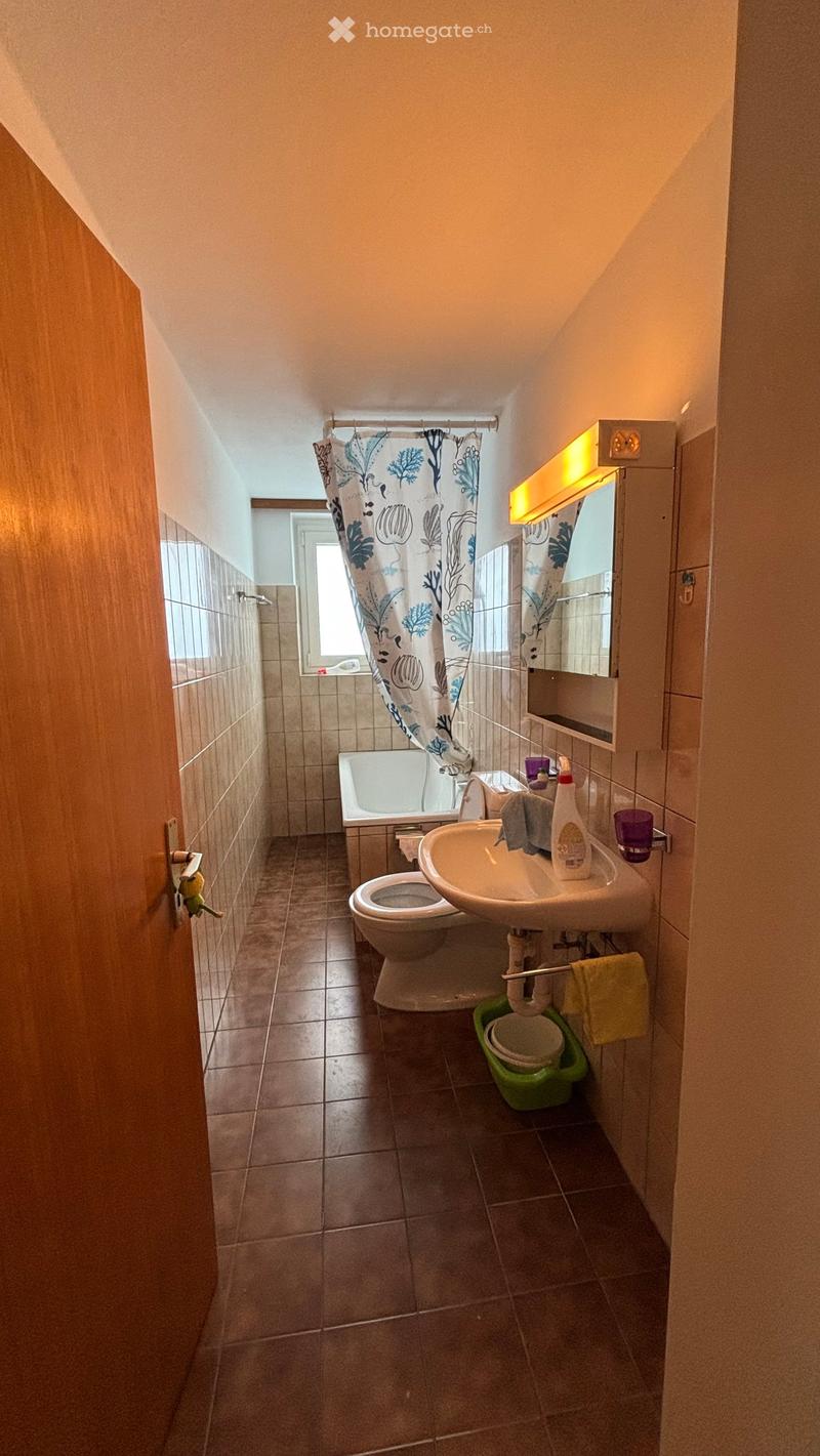 Bathroom with tiled walls and floor, featuring a bathtub, toilet, sink, mirror, and various toiletries.