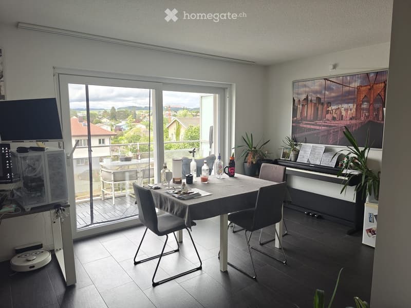 Modern dining area with a table, chairs, piano, and a large window offering a scenic view of the landscape.