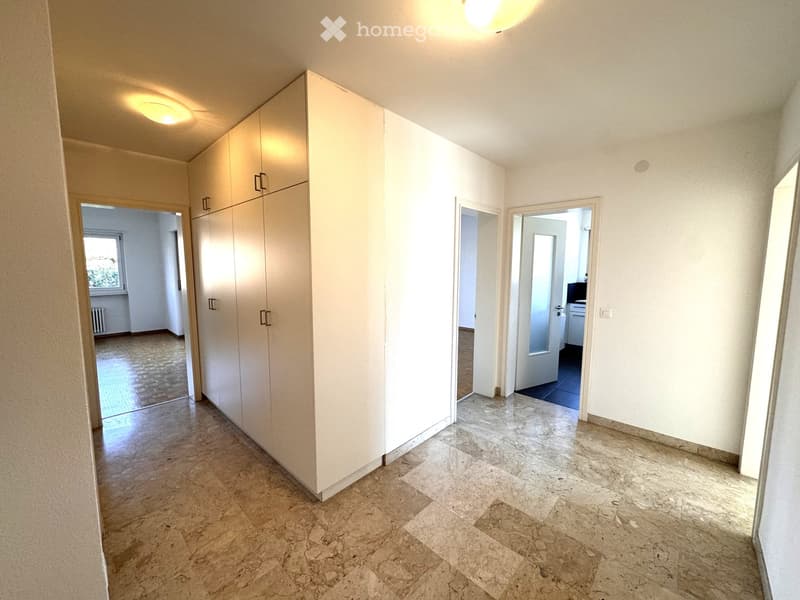 Empty hallway with white walls, marble flooring, built-in white closet, and recessed lighting. Three doors lead to other rooms.