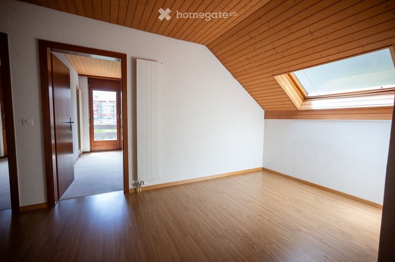 Empty room with wooden flooring, white walls, and wooden ceiling. Features a skylight window and an open doorway leading to a hallway.