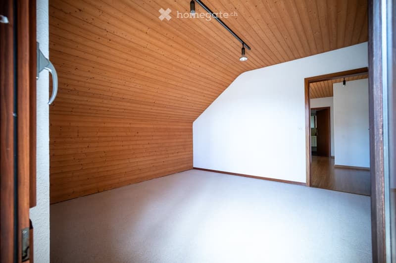 Empty room with wooden walls, white walls, and a wooden ceiling. The floor is light-colored, and there are no visible furnishings or decorations.