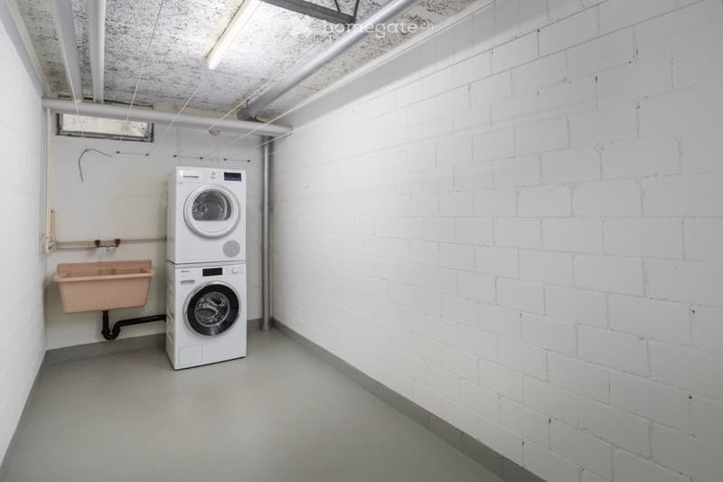 A small utility room with white brick walls, a washing machine, and a sink.