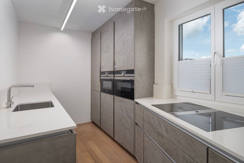 Modern kitchen with white countertops, stainless steel sink, built-in oven, and grey cabinets.
