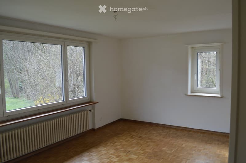 Empty room with wooden flooring, white walls, large windows, radiator, and a small window sill.