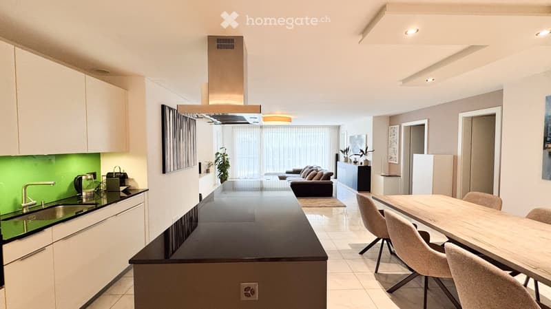 Modern kitchen with white cabinets, black countertop, and a dining area with a wooden table and chairs. The living area features a sofa, plants, and large windows with curtains.