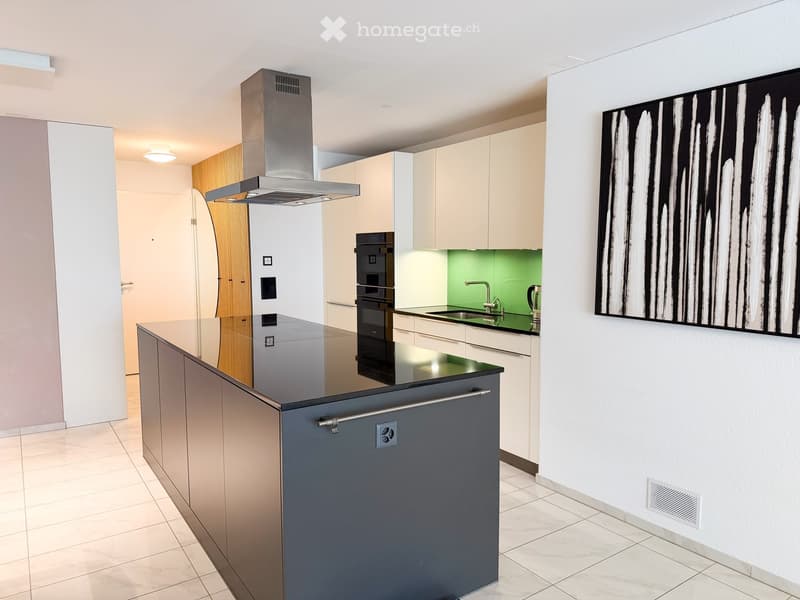 Modern kitchen with light-colored cabinets, stainless steel appliances, a central island, and a sleek black countertop.