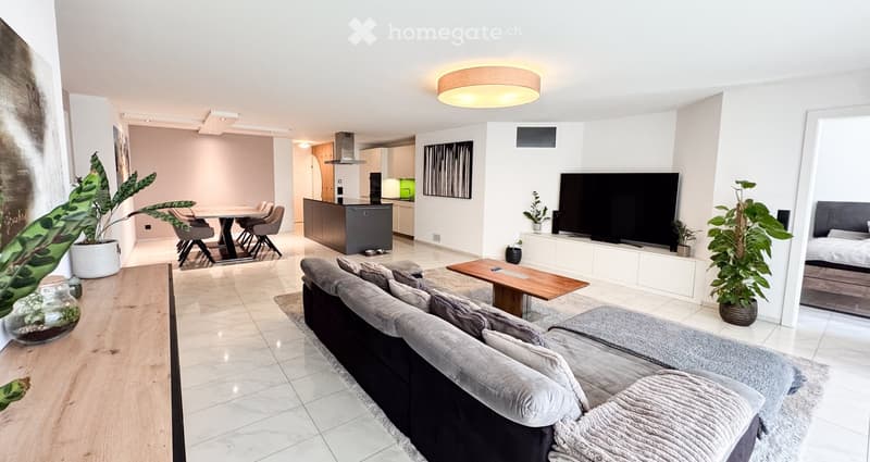 Modern open-plan living and dining area with a grey sofa, coffee table, flat-screen TV, dining table with chairs, and a kitchen island.