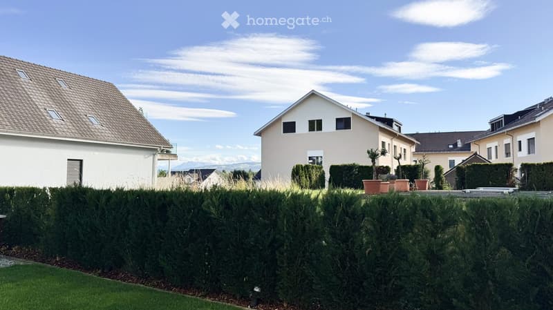 Residential houses with modern architecture, surrounded by neatly trimmed hedges and potted plants.