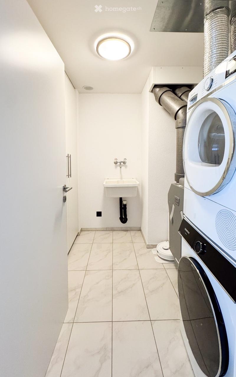 Modern bathroom with white tiled floor, white walls, a sink with a faucet, and a stacked washing machine and dryer unit.