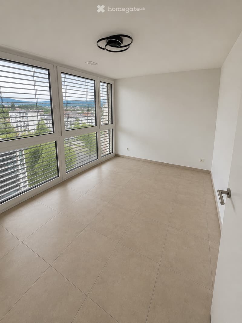 Empty room with beige tiled floor, white walls, large windows with blinds, and a modern ceiling light fixture.