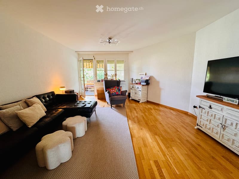 Modern living room with a black leather sofa, ottoman, armchair, small table, TV, and decorative items on a side table.