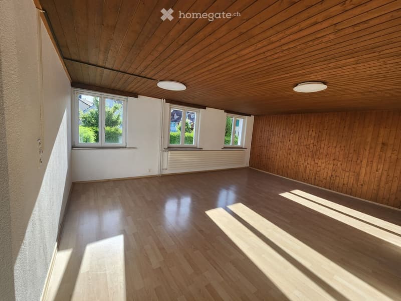 Empty room with wooden flooring, white walls, and wooden ceiling. Three windows provide natural light, and there is a radiator on one wall.