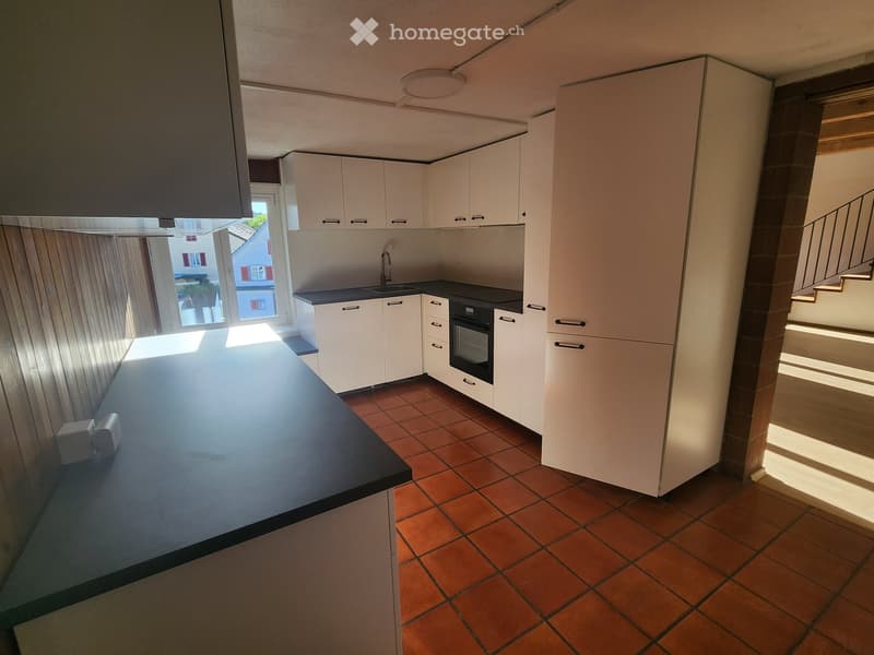 Modern kitchen with white cabinets, black countertops, and a central island. Features a sink, oven, and a window with blinds.