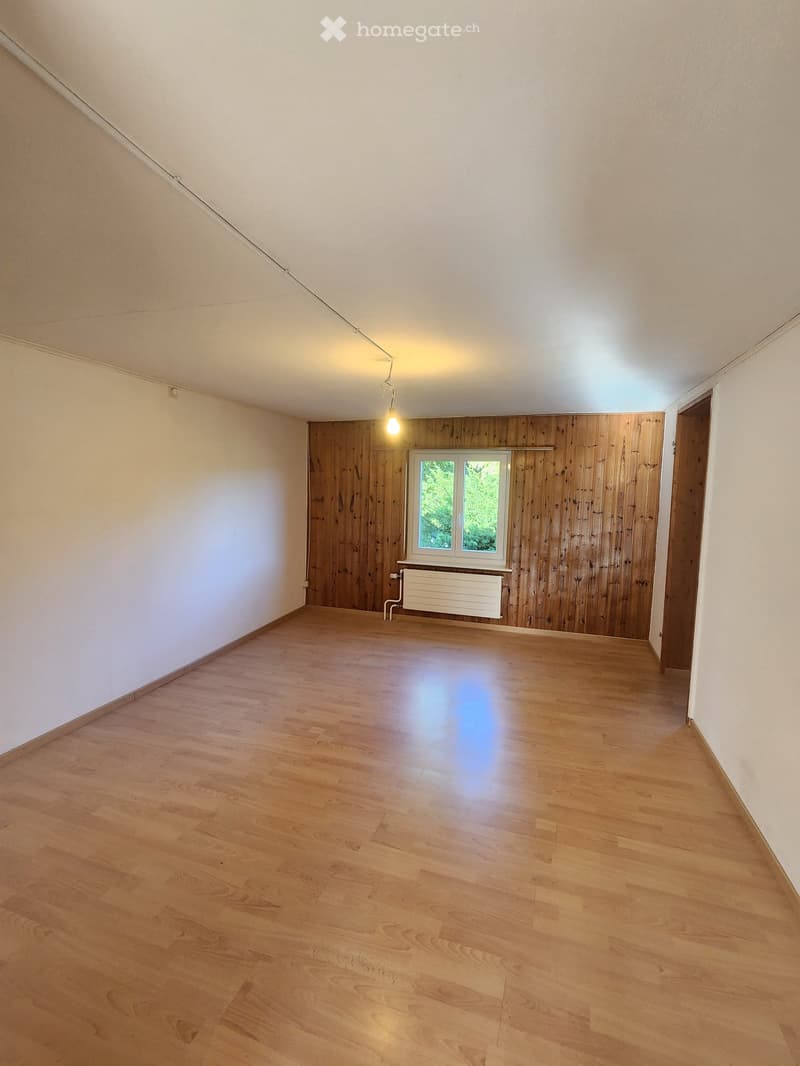 Empty room with wooden flooring, white walls, and a single window with wooden paneling on one wall.