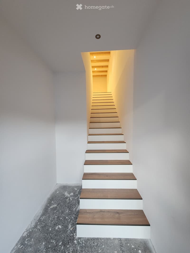 Modern staircase with wooden steps and white risers, leading upwards with soft lighting at the top.