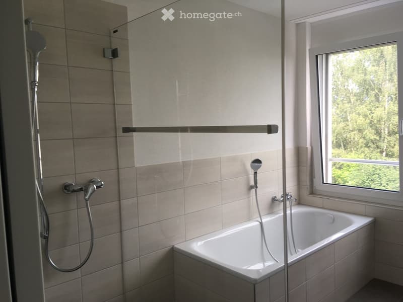 Modern bathroom with a bathtub, showerhead, and a window overlooking greenery.