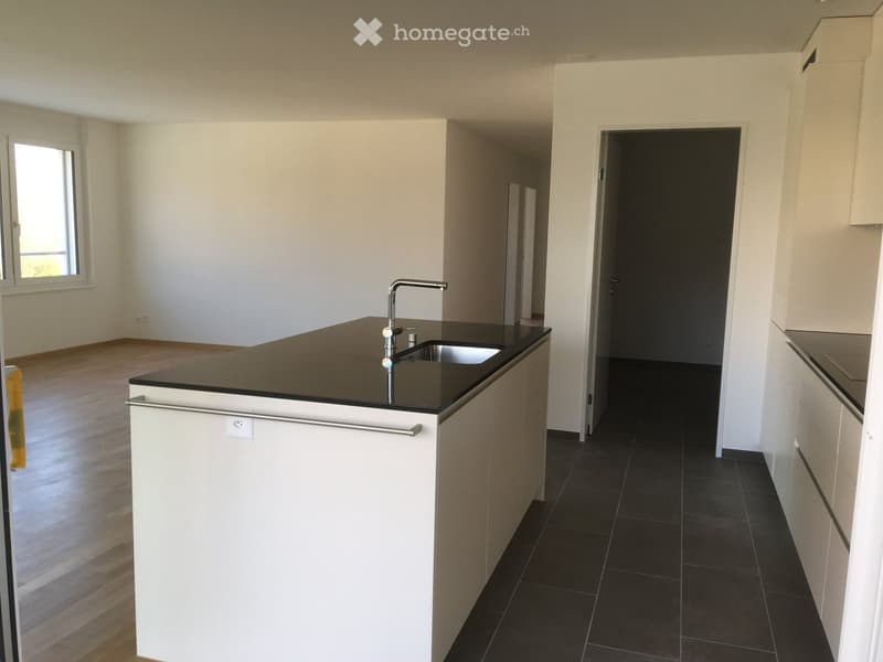 Modern kitchen with white cabinets, black countertops, and a stainless steel sink. The floor is dark tiled, and the walls are white.