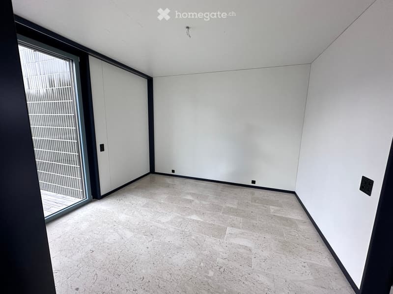 Empty room with white walls, light grey tiled floor, and large glass sliding door leading outside.