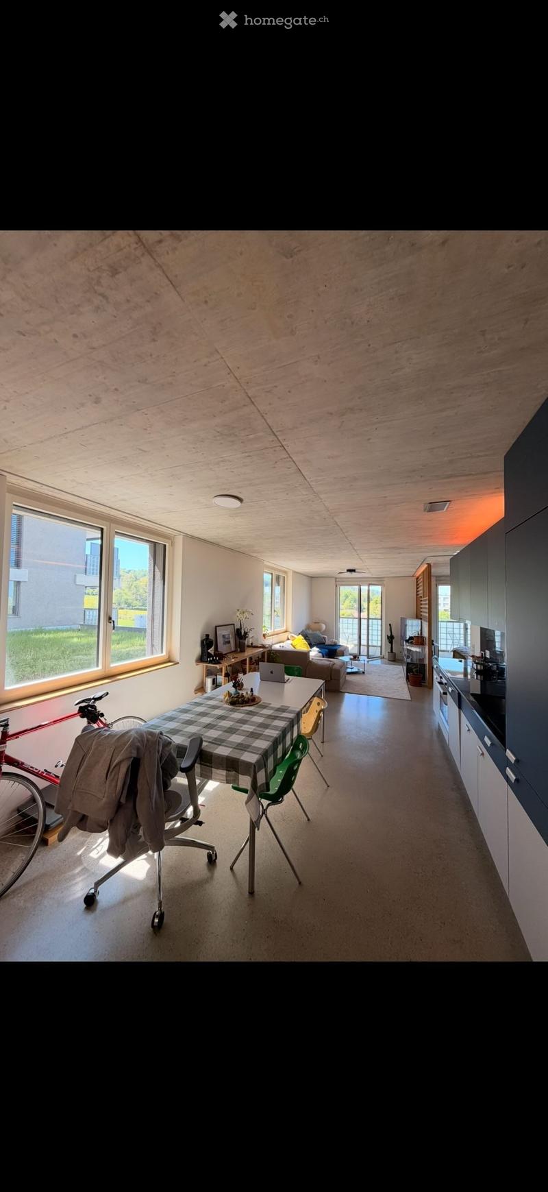 Open-plan living and dining area with modern kitchen, large windows, and wooden ceiling.