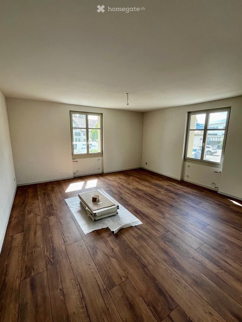 Empty room with wooden flooring, two windows, and a small wrapped item on the floor.