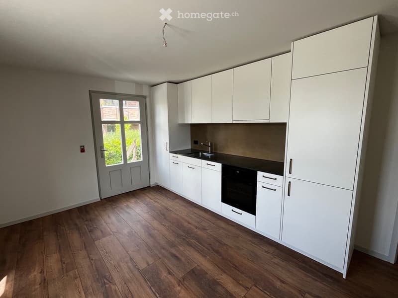 Modern kitchen with white cabinets, wooden flooring, and a black countertop. Features a sink, faucet, and built-in oven.