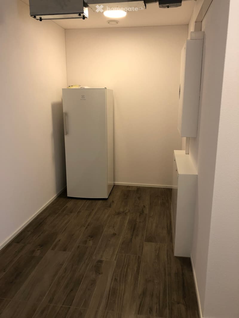 Empty room with wooden flooring, white walls, and a small refrigerator in the corner.