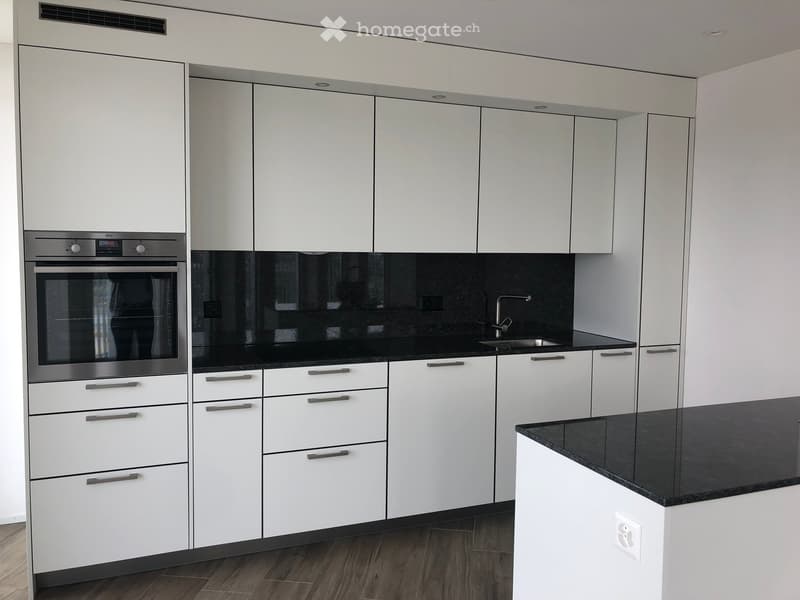 Modern kitchen with white cabinets, black countertops, and stainless steel appliances including an oven and sink.