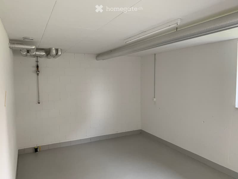 Empty room with white walls, grey floor, exposed pipes, and a single window