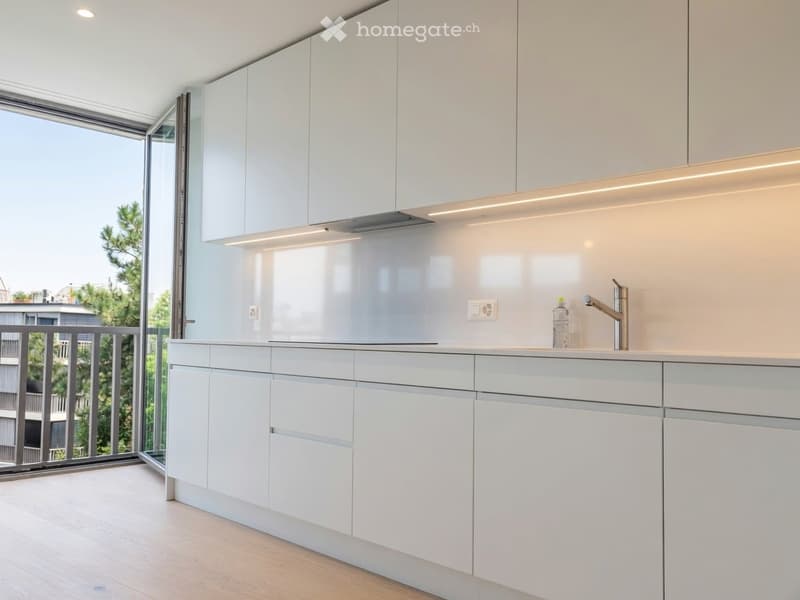 Modern kitchen with white cabinets, sleek countertops, and a large window offering a view of greenery.