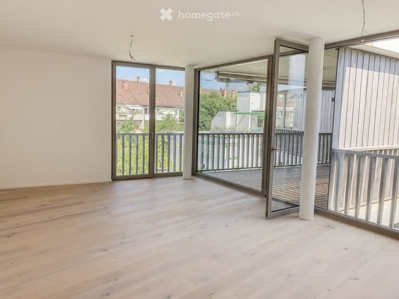 Empty room with wooden flooring, large glass doors leading to a balcony, and a view of the surrounding area.