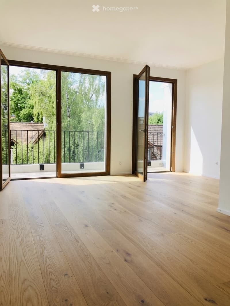 Empty room with light wooden flooring and large sliding glass doors leading to a balcony.