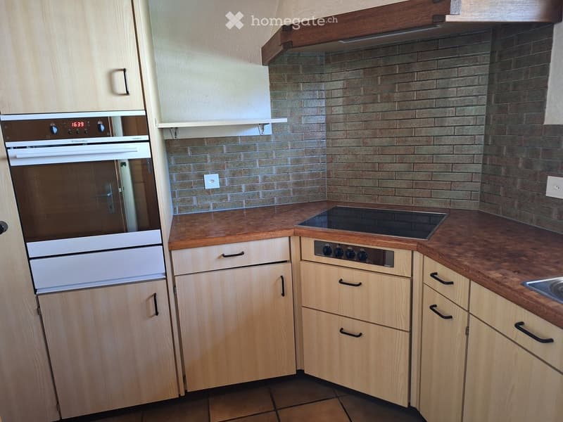 Modern kitchen with light wooden cabinets, an oven, an induction stove, and a tiled backsplash.