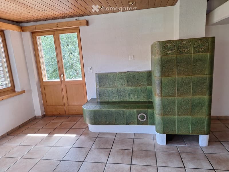 Bathroom with a green tiled bathtub, wooden door, and window with a view of greenery.