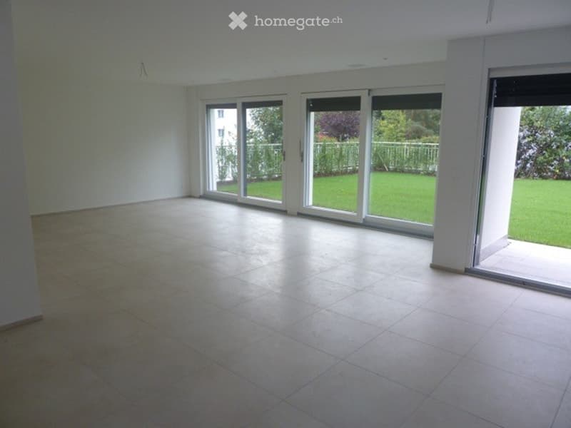 Empty room with large sliding glass doors leading to a green garden, tiled floor, white walls, and bright natural lighting.