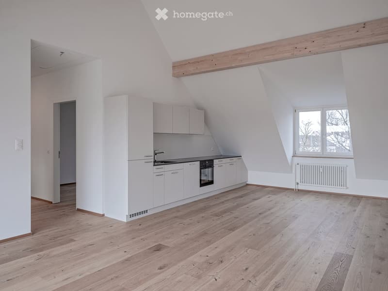 Bright, modern kitchen with white cabinets, a sink, an oven, and wooden flooring. Large windows provide natural light, and a radiator is visible on the wall.