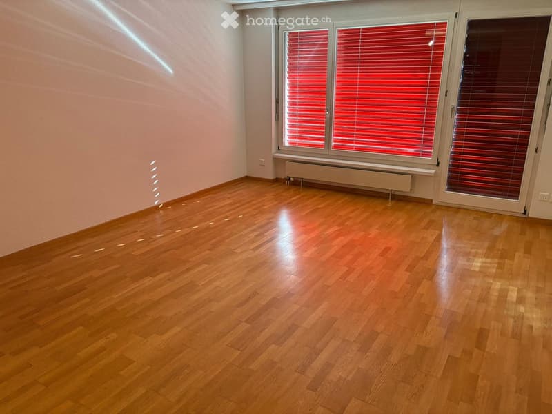 Empty room with wooden flooring, white walls, and large windows with red blinds. No furniture or equipment present.