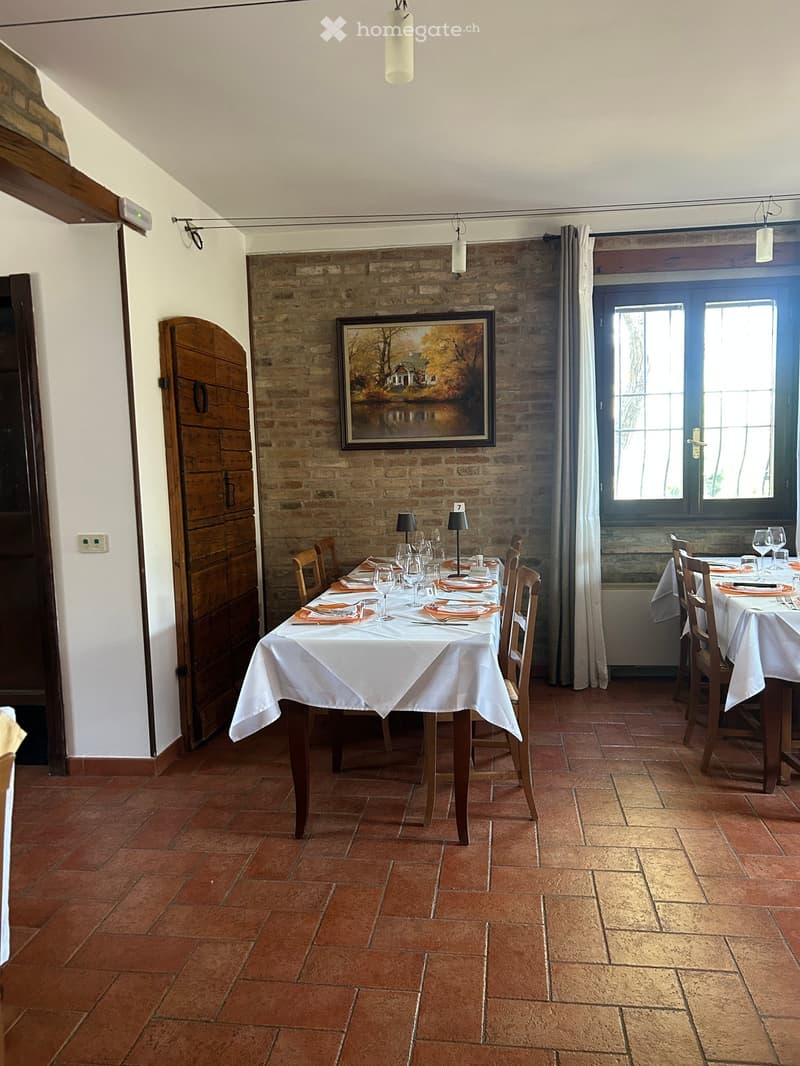 Dining room with exposed brick walls, terracotta tiled floor, and two dining tables set for guests.